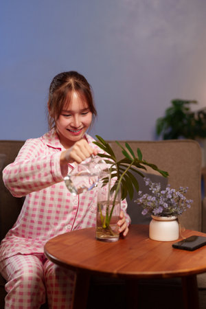 Asian adult woman caring for plant indoors, promoting wellness and a balanced lifestyle. A simple act of self-care for a calm and healthy living environment.の写真素材