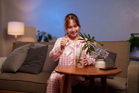 Young Asian woman smiling while carefully watering plant vase to enhance home decor creating a joyful moment, improve wellbeing, brings positive energy, and healthy lifestyle.の写真素材