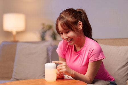 An adult Asian woman smiling using aromatherapy diffuser to enhance her wellbeing at home A simple way to add self-care practice into the daily routineの写真素材