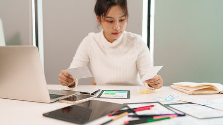 Asian adult woman is working as user interface designer sketching website layout with mobile application interface wireframes for a digital project development.の写真素材
