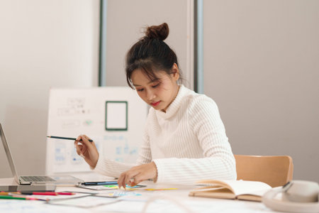 Young Asian woman designs mobile app and website UI UX at her desk She works with user interface and...