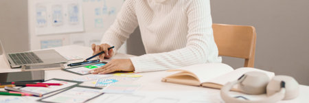 Asian adult woman's hands are designing mobile app interface on tablet for good user experience. Focus on website wireframe creation in design process on the table.の写真素材
