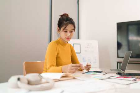 This Asian young UI designer creates awesome mobile app interface layout ideas working at her desk with laptop to develop website or application design.の写真素材