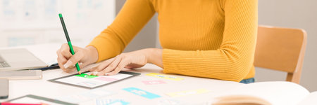 An Asian adult women is hands on designing a user interface with a pencil on a tablet. Focusing on website and app development UX strategy.の写真素材