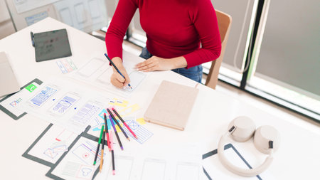 This image features an adult Asian woman UI designer creating mobile app wireframes and prototypes...