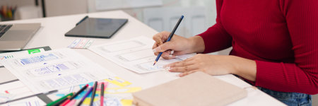 An adult Asian women UI designer is sketching mobile app interface design on paper with a pencil at the office for website and application project.の写真素材