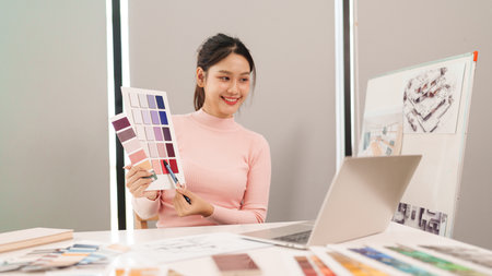 Adult Asian woman user interface designer presents color samples for website design during a video conference. Working on a computer for an online meeting.の写真素材