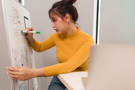 Young Asian UI designer is planning mobile application design brainstorming on whiteboard for color...