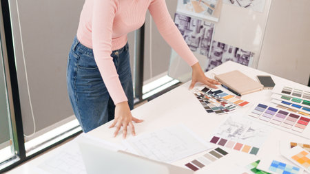 Asian adult woman choosing a color palette from swatches on the desk for a user interface design. Woman creating layout on the desk for website or mobile app design.の写真素材