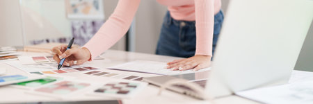 An adult Asian woman interior designer is working on a home decor project. She is choosing a color palette and creating a design using a laptop. She is a young UI UX designer.の写真素材