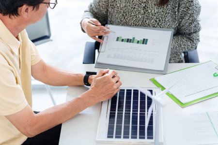 Asian business professionals examine sustainability reports on renewable energy and environmental...