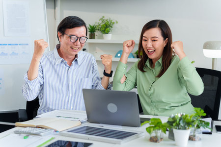 Happy Asian male and female colleagues celebrate a significant business victory achieving sustainable environmental social governance targetsの写真素材