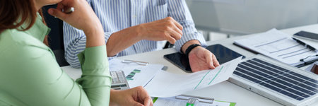 Two adult Asian business professionals engaged in an ESG discussion analyzing financial data for...