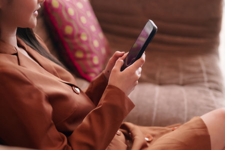 Confident Asian adult woman utilizes smartphone from home. She embodies modern professional digital connection. Empowering her busy lifestyle with technology.の写真素材