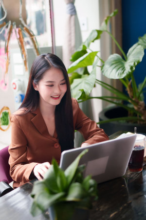 Confident Asian female works efficiently on her portable computer in a chic coffee shop for professional development and online networkingの写真素材