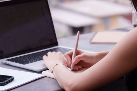 Focused professional hands meticulously documenting ideas on a notebook near a laptop showcasing modern remote work flexibility and smart connectivityの写真素材
