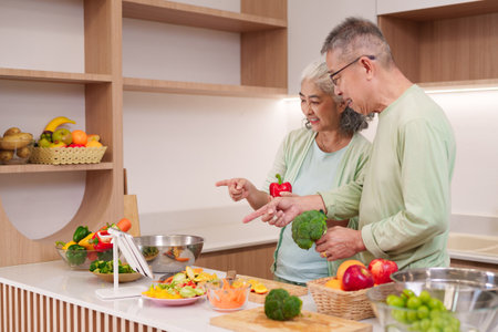 Happy Asian older adults preparing delicious healthy meal together bright modern kitchen. Fresh ingredients promote wholesome eating wellness.の写真素材