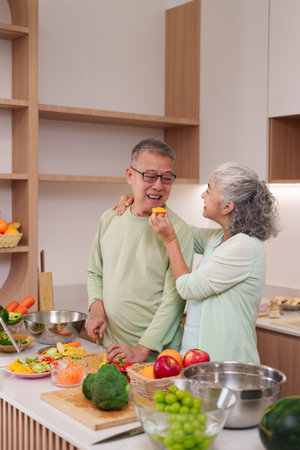 Happy Asian senior couple preparing nutritious food in their modern kitchen. They share a tender...