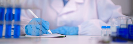 Adult scientist hand in protective blue glove records experiment data in spiral notebook for medical chemical biological research at lab facility.の写真素材
