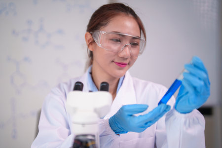 Focused Asian adult woman scientist holds a test tube with blue liquid doing lab research developing new medical breakthroughs professional studyの写真素材