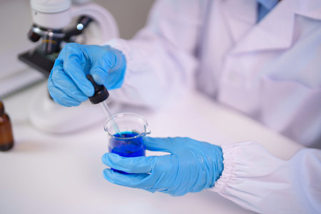 Adult scientist hands perform precise chemical analysis using dropper and beaker in a modern...