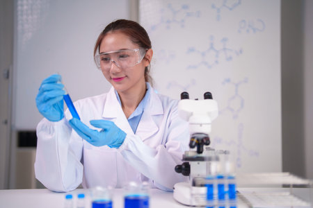 Adult Asian female scientist analyzing blue solution in test tube during scientific experiment....
