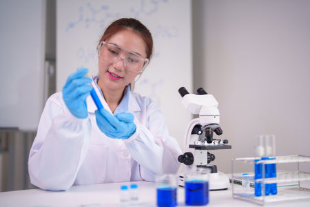 Asian adult woman scientist conducts chemical analysis using test tube microscope modern laboratory setting professional research workの写真素材