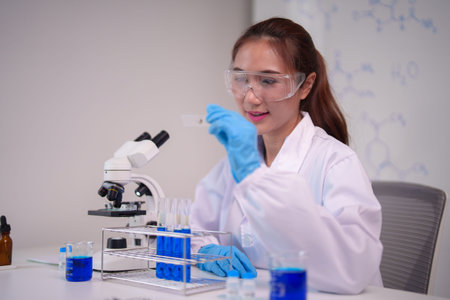 Adult Asian female researcher examining slide with protective gear lab setting science equipment for...