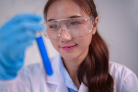Diligent Asian adult scientist conducts an important experiment analyzing a blue liquid She wears...
