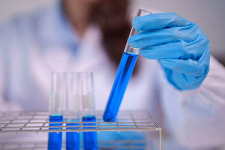 Adult hand in blue glove holds a test tube with vibrant blue liquid performing precise laboratory...