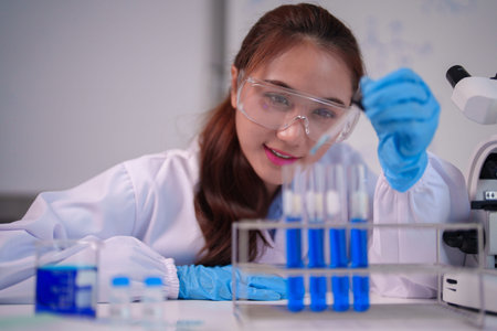 Focused Asian female scientist performs precise liquid transfer with a pipette into test tubes at a modern science laboratory Her diligent work promotes discoveryの写真素材