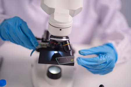Adult hands in blue gloves adjust specimen slide under microscope conducting precise scientific...