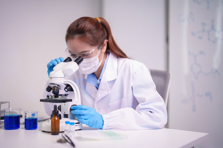Adult Asian female researcher investigates unknown substances using advanced laboratory microscope discovers solutions for complex biological challengesの写真素材