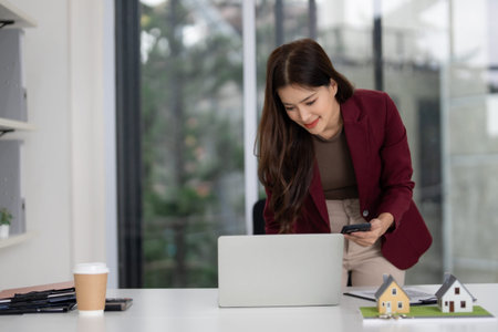 Adult Asian woman realtor busy with property transactions. She connects with clients using...