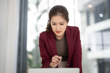 Asian businesswoman diligently working on computer. Dedicated real estate professional examining property data. Strategic planning for successful sales. Focused client needs.の写真素材