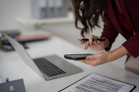 Adult professional hands operate smartphone with pen near laptop document managing real estate sales...