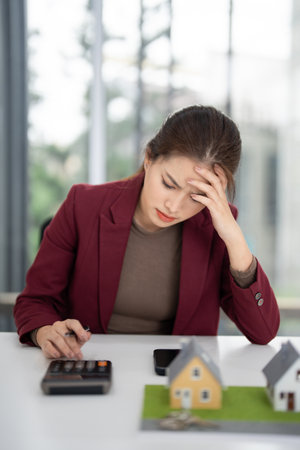 Adult Asian woman realtor confronts complex financial decisions regarding property investment her expression reveals deep concern on white deskの写真素材