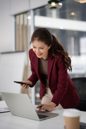 Professional Asian businesswoman engages in real estate tasks using modern technology to connect with clients and manage property listings with a joyful attitudeの写真素材