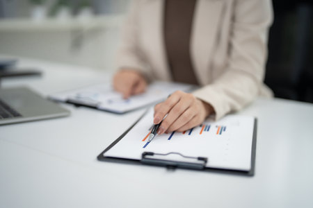 Professional adult Asian hand points to financial chart on report. Business person analyzes market trends for real estate planning.の写真素材