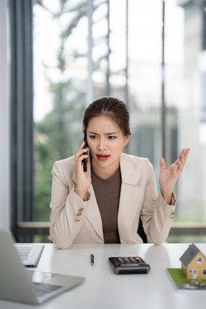 Adult Asian agent consults client real estate property issue via phone professional office setting managing financial sales transactionの写真素材