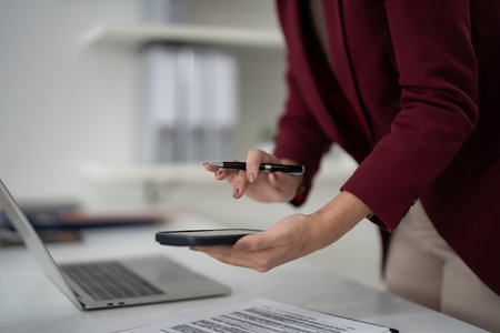 Adult hands engage mobile phone with pen. A real estate professional manages important sales paperwork using modern office technology.の写真素材
