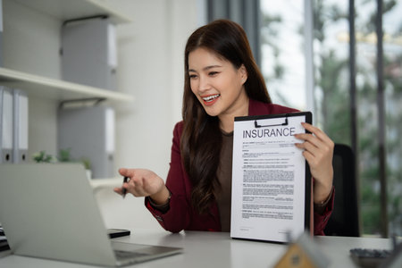 Asian professional discusses insurance details via video conference She explains property protection plans from a contemporary office setting connecting clientsの写真素材