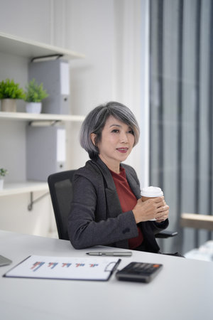 Experienced Asian corporate leader enjoys a brief coffee break. Thoughtfully planning strategy at...