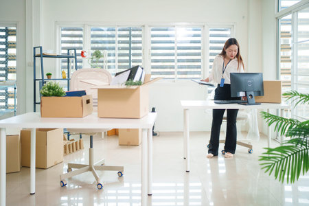 Adult Asian man smiling placing potted plant into cardboard box. Setting up new office space....