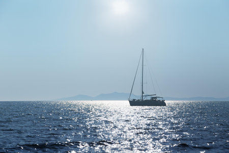 Silhouette of the yacht at sea on the background of the island and bright sun.