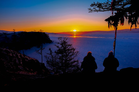 Silhouette of two people sitting on the top of the mountain and watching the sunrise,at Lake Baikal,Siberia, Russiaの写真素材
