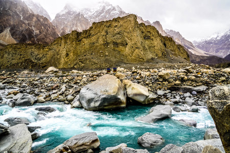 Turquoise water flowing in hunza river with Rainbow Suspension bridge, Passu cones and thick clouds in view,north Pakistanの写真素材
