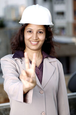 Smiling young Indian female architect showing victory signの写真素材