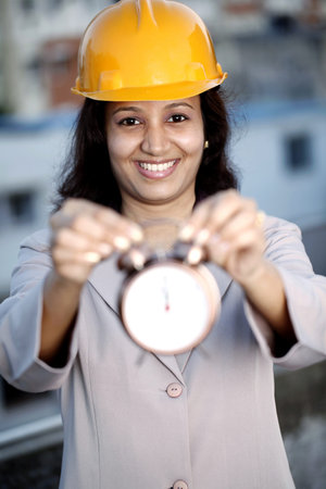 Smiling young female construction engineer holding alarm clockの写真素材