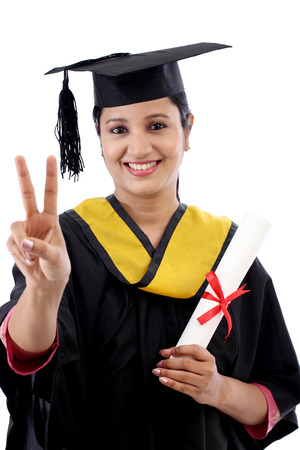 Smiling young graduation student making thumbsup gesture against whiteの写真素材